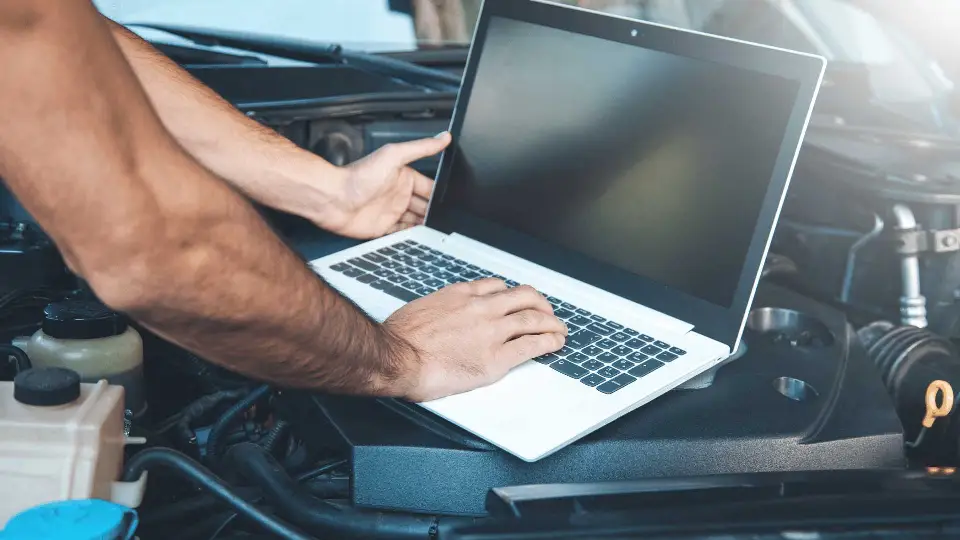 Technician running diagnostics on a laptop over an open engine bay